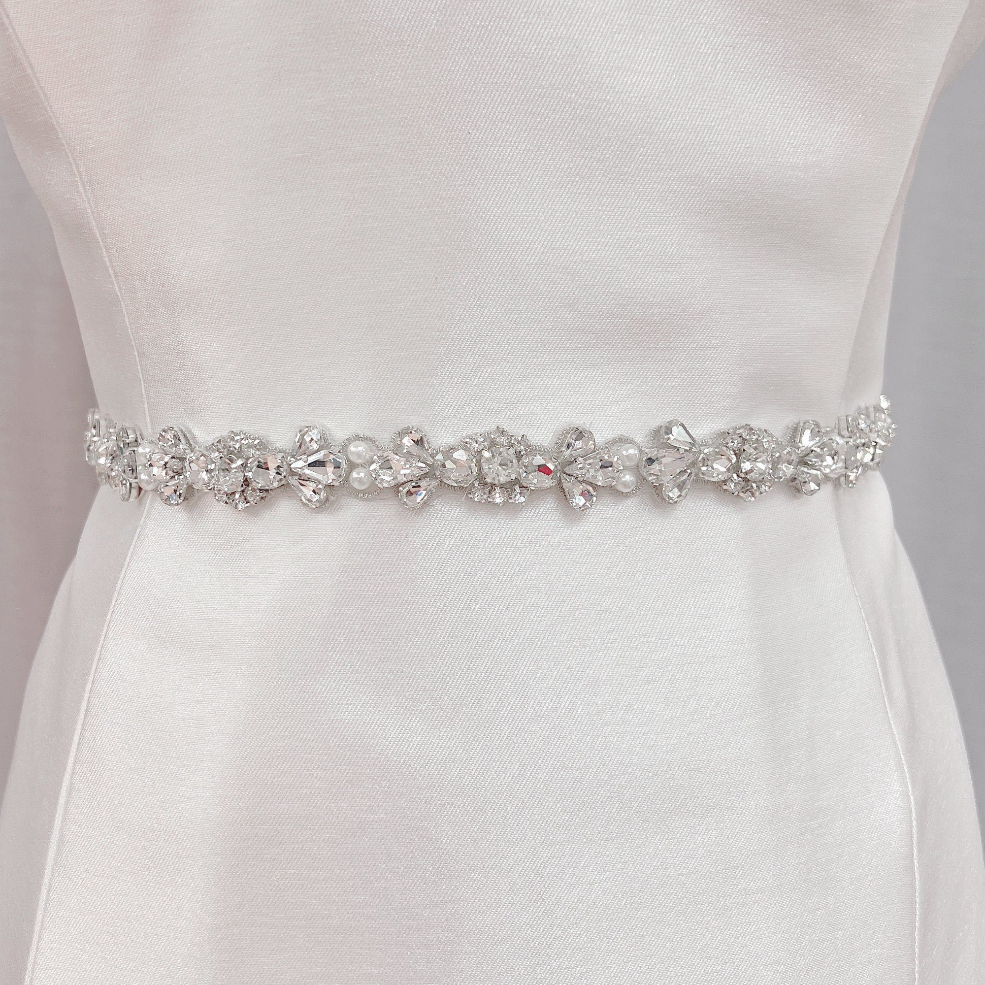 Handmade rhinestone and pearl bridal belt displayed on a dress form to showcase the intricate crystal beadwork.