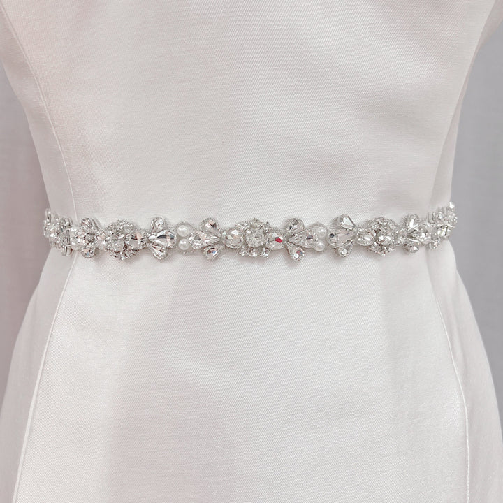 Handmade rhinestone and pearl bridal belt displayed on a dress form to showcase the intricate crystal beadwork.