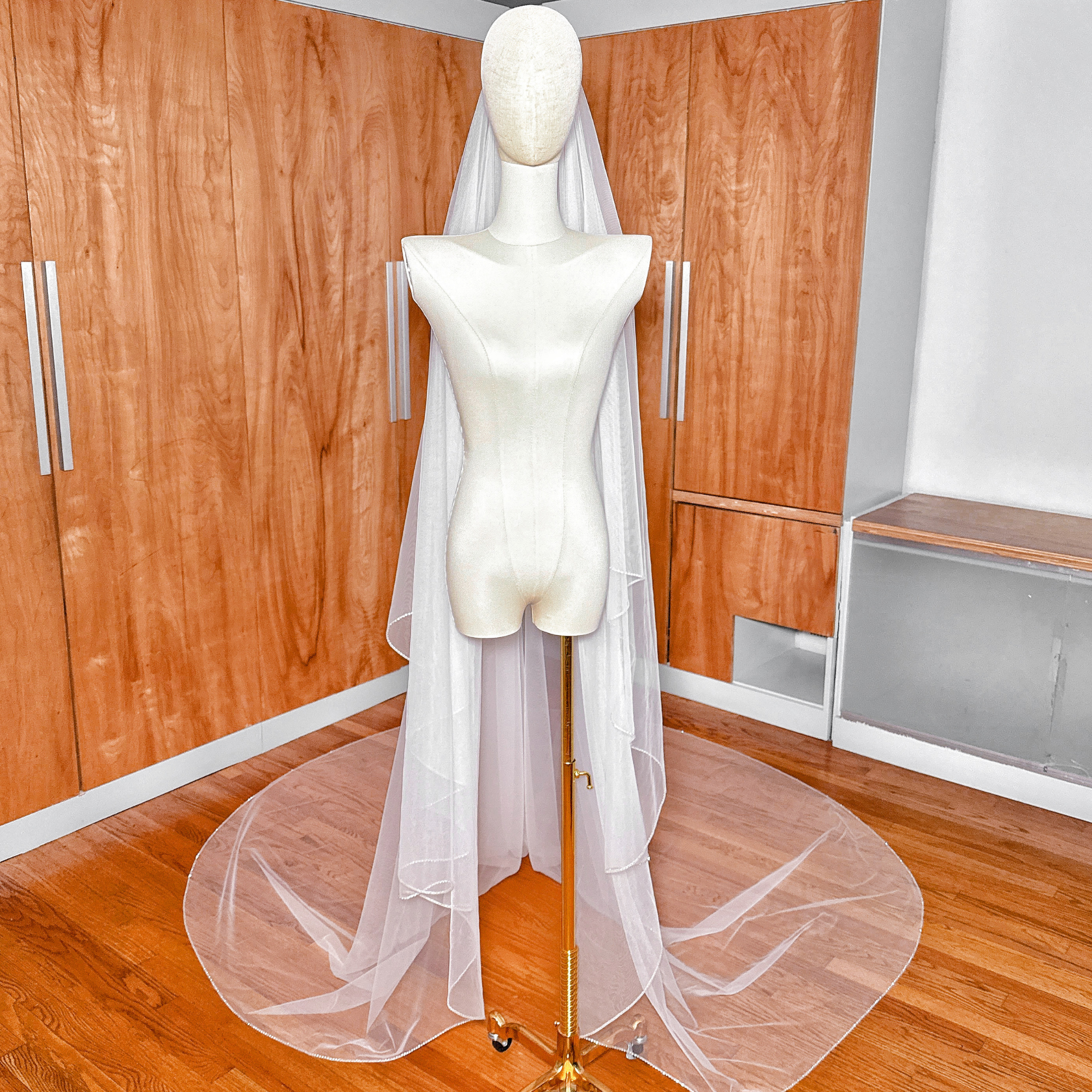 Ground-level view showing the wide, elegant curve of the rhinestone edge along the hemline of a cathedral length two-tier wedding veil.