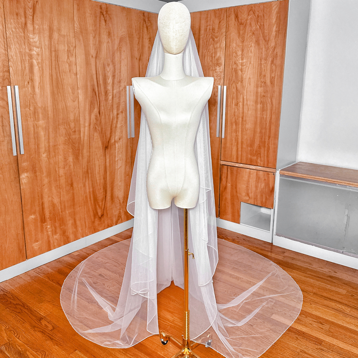 Ground-level view showing the wide, elegant curve of the rhinestone edge along the hemline of a cathedral length two-tier wedding veil.