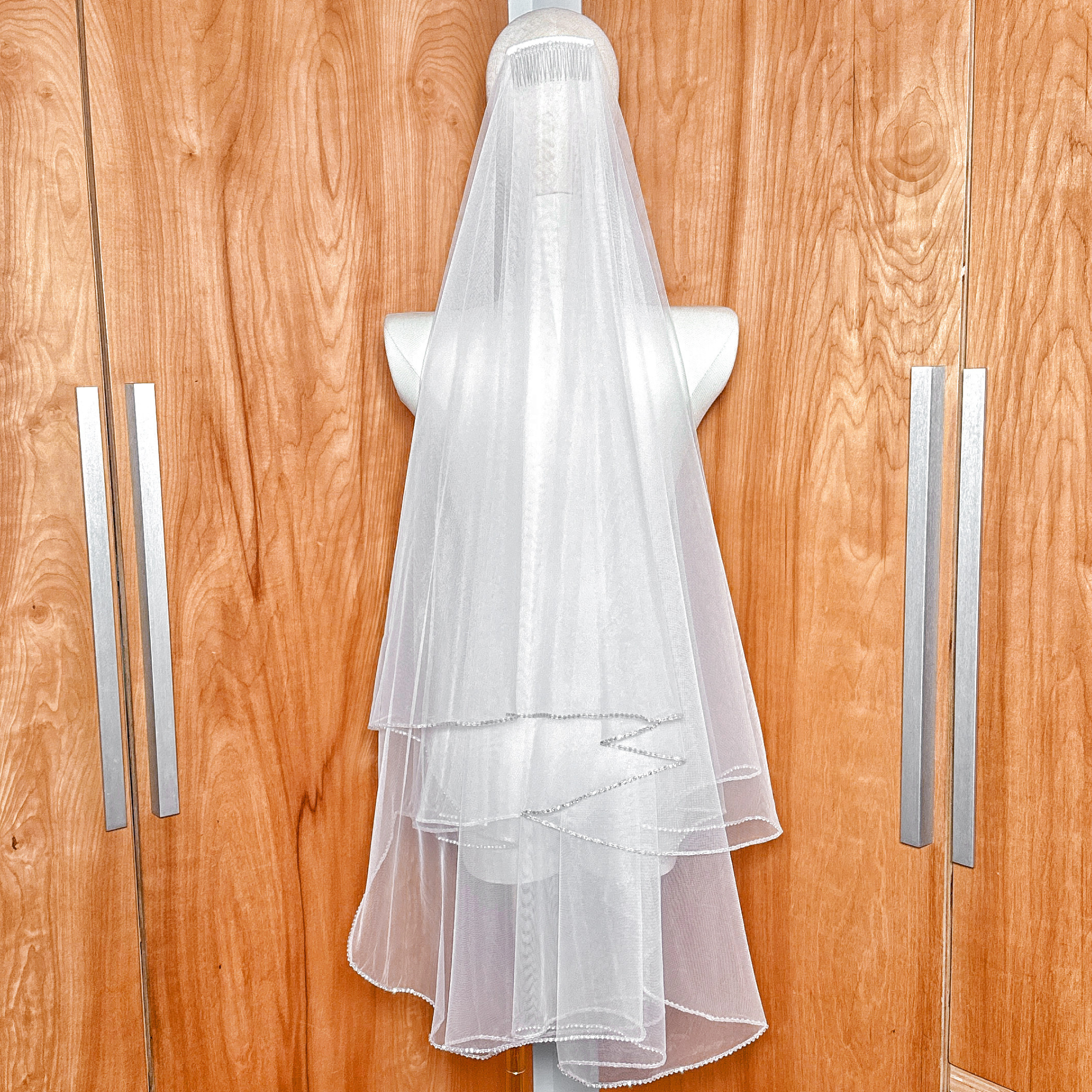 Close-up of a two tier wedding veil featuring a detailed rhinestone edge in fingertip length.