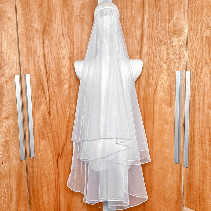Close-up of a two tier wedding veil featuring a detailed rhinestone edge in fingertip length.