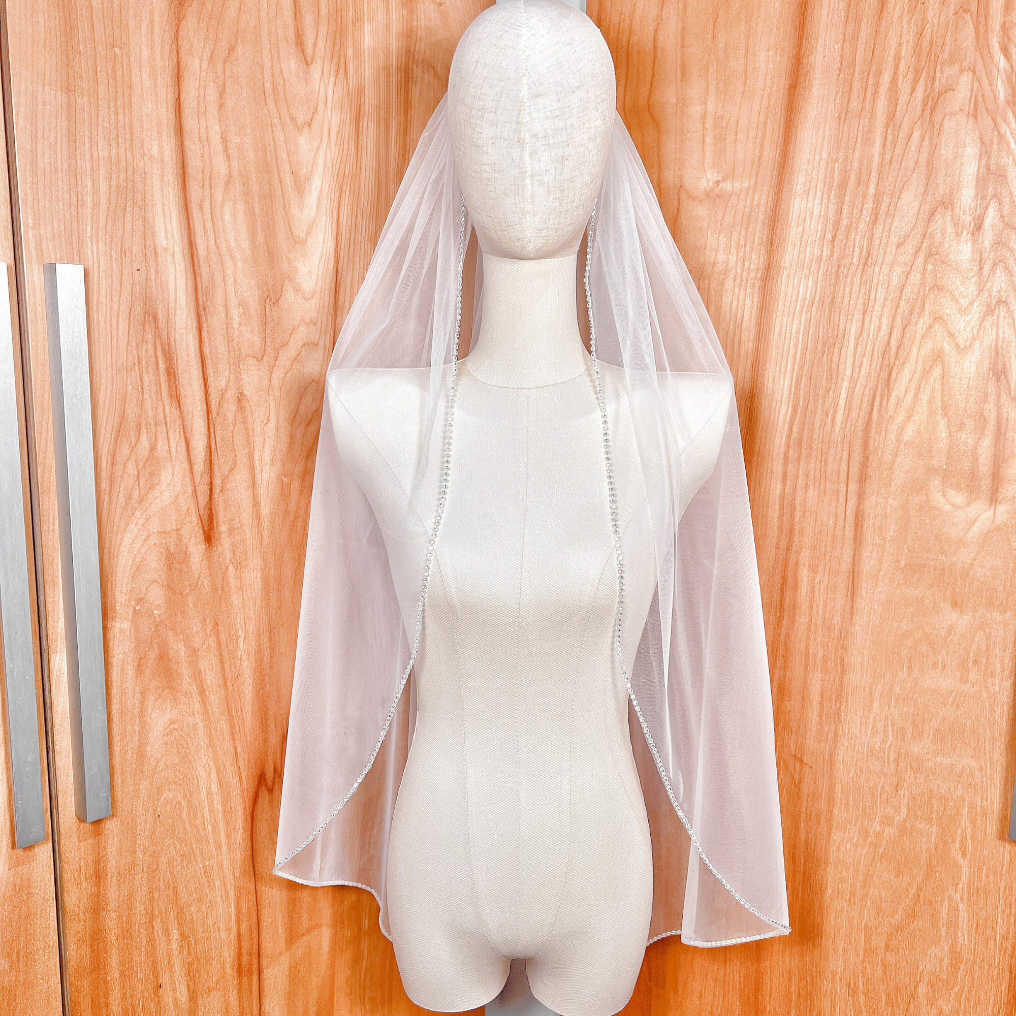 Fingertip length rhinestone edge wedding veil displayed on a bridal mannequin.
