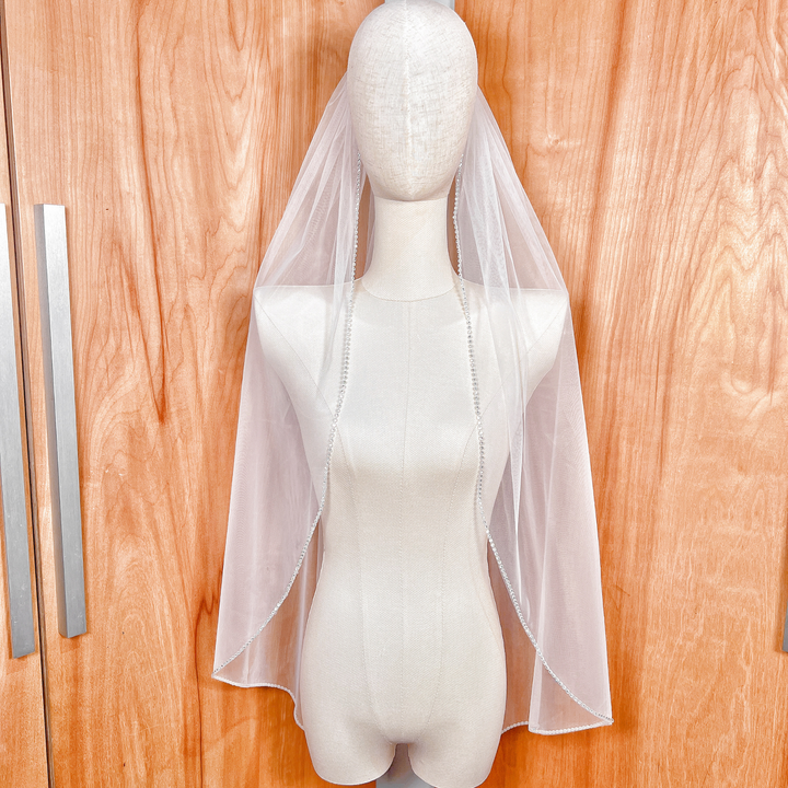 Fingertip length rhinestone edge wedding veil displayed on a bridal mannequin.