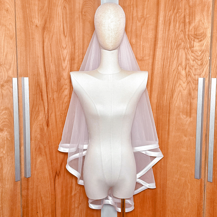 Fingertip length wedding veil with a wide ribbon edge and blusher, styled on a bridal mannequin.