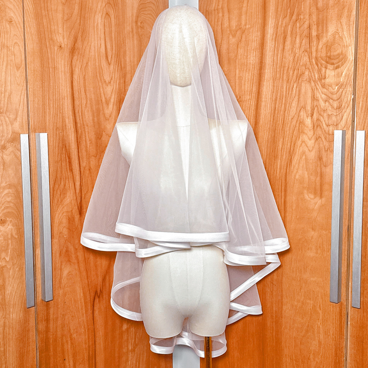 Front view of a fingertip length bridal veil with a one-inch ribbon edge and blusher displayed on a mannequin.