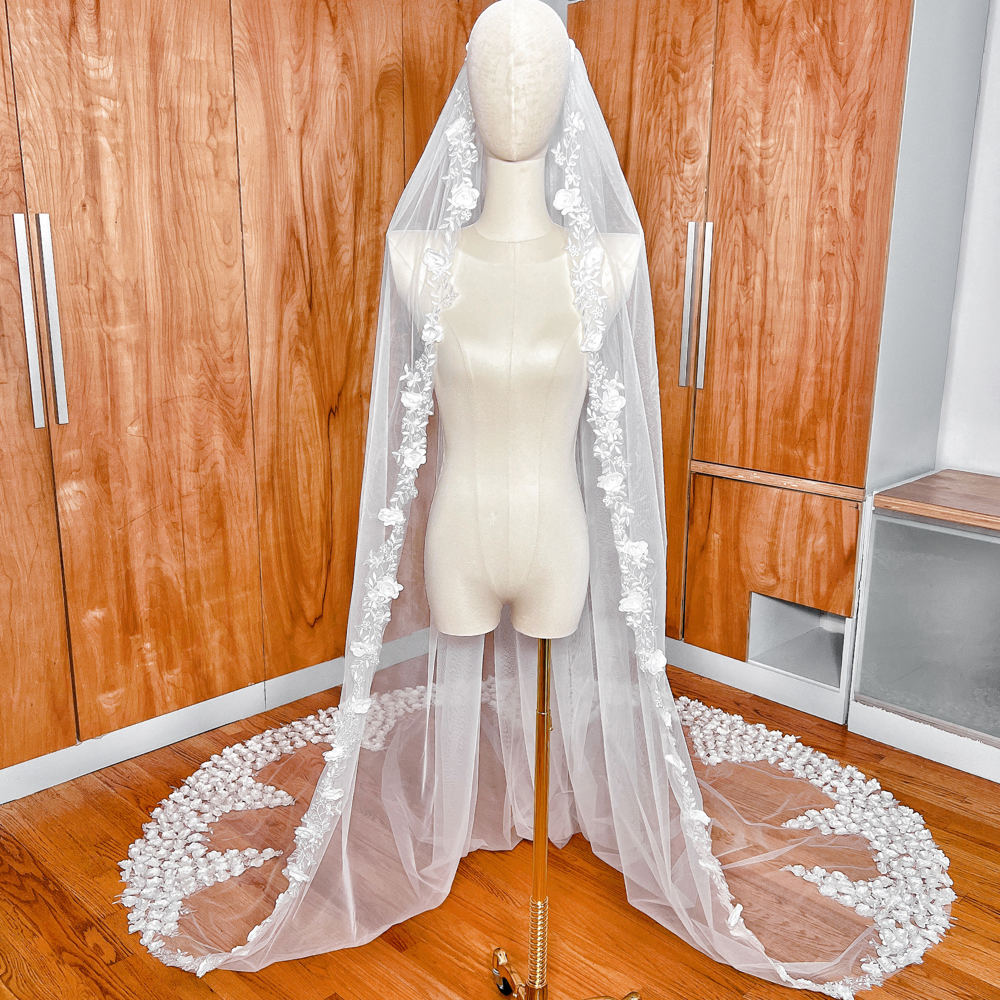 A cathedral-length romantic 3D flower wedding veil with delicate floral appliqués displayed on a professional mannequin, front view.