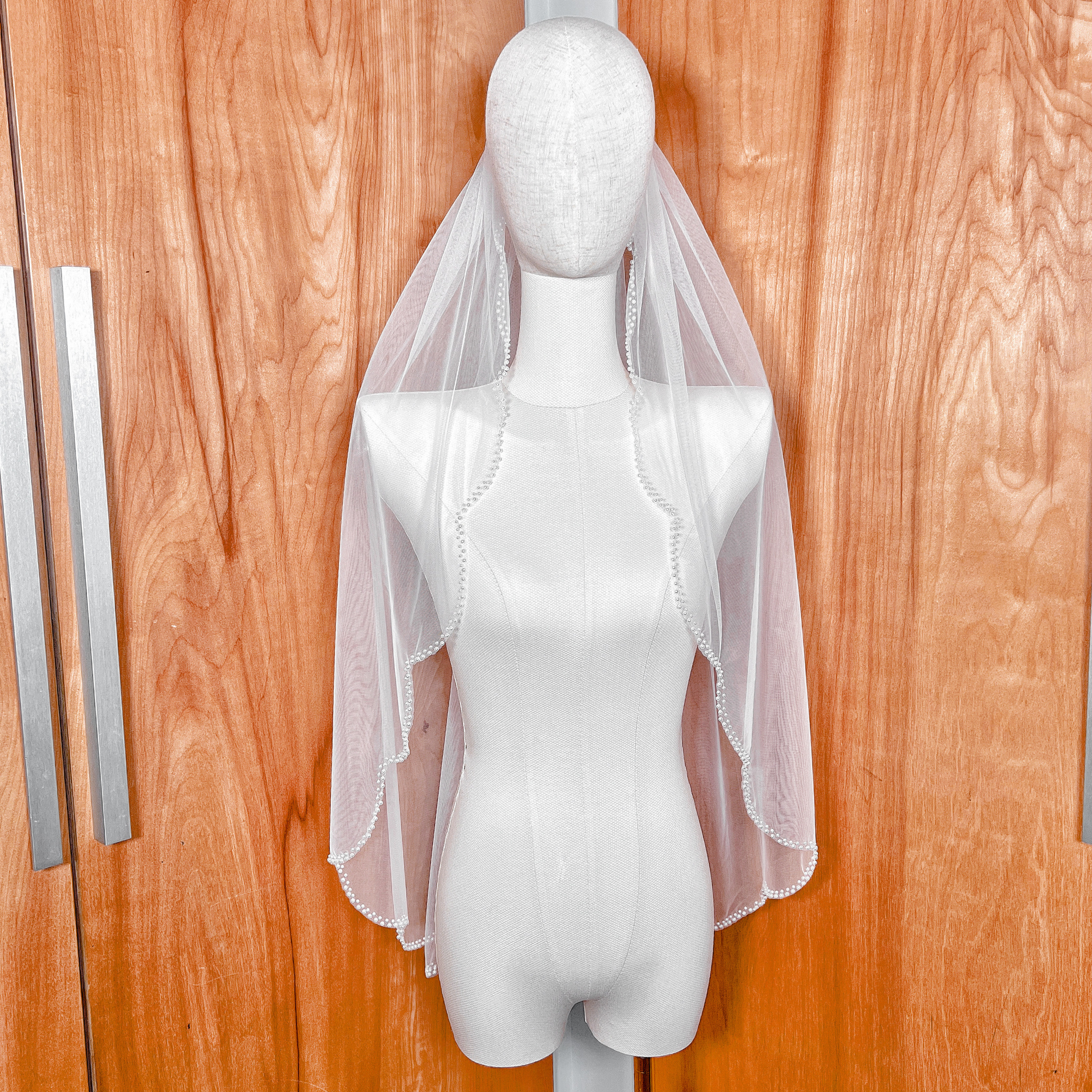 A single-tier ivory scalloped wedding veil with a delicate pearl edge shown in fingertip length.