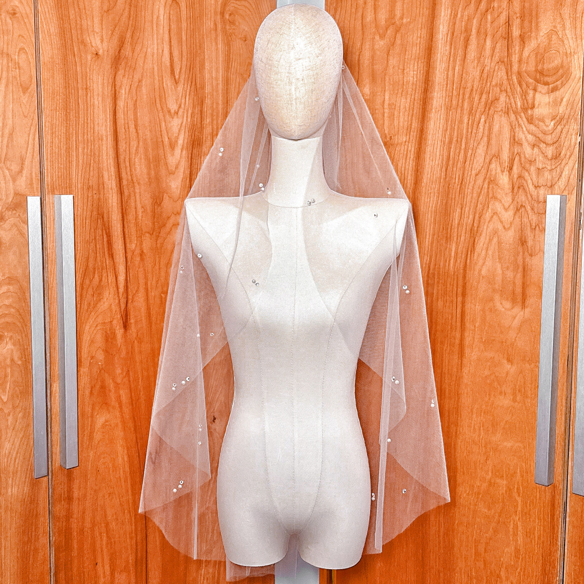 A fingertip-length wedding veil made of sheer tulle with scattered pearls and rhinestones.