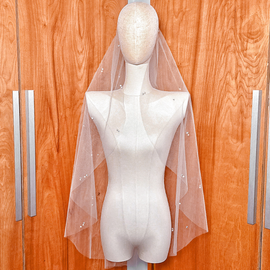 A fingertip-length wedding veil made of sheer tulle with scattered pearls and rhinestones.