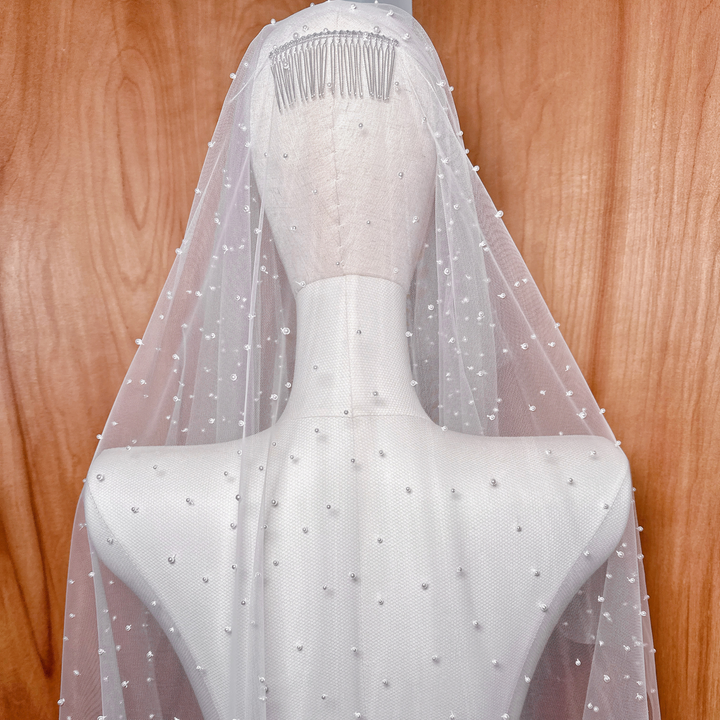 Close-up detail of hand-applied pearls on the scattered pearl blusher veil, emphasizing the sheer texture of the knee-length tulle on a mannequin.