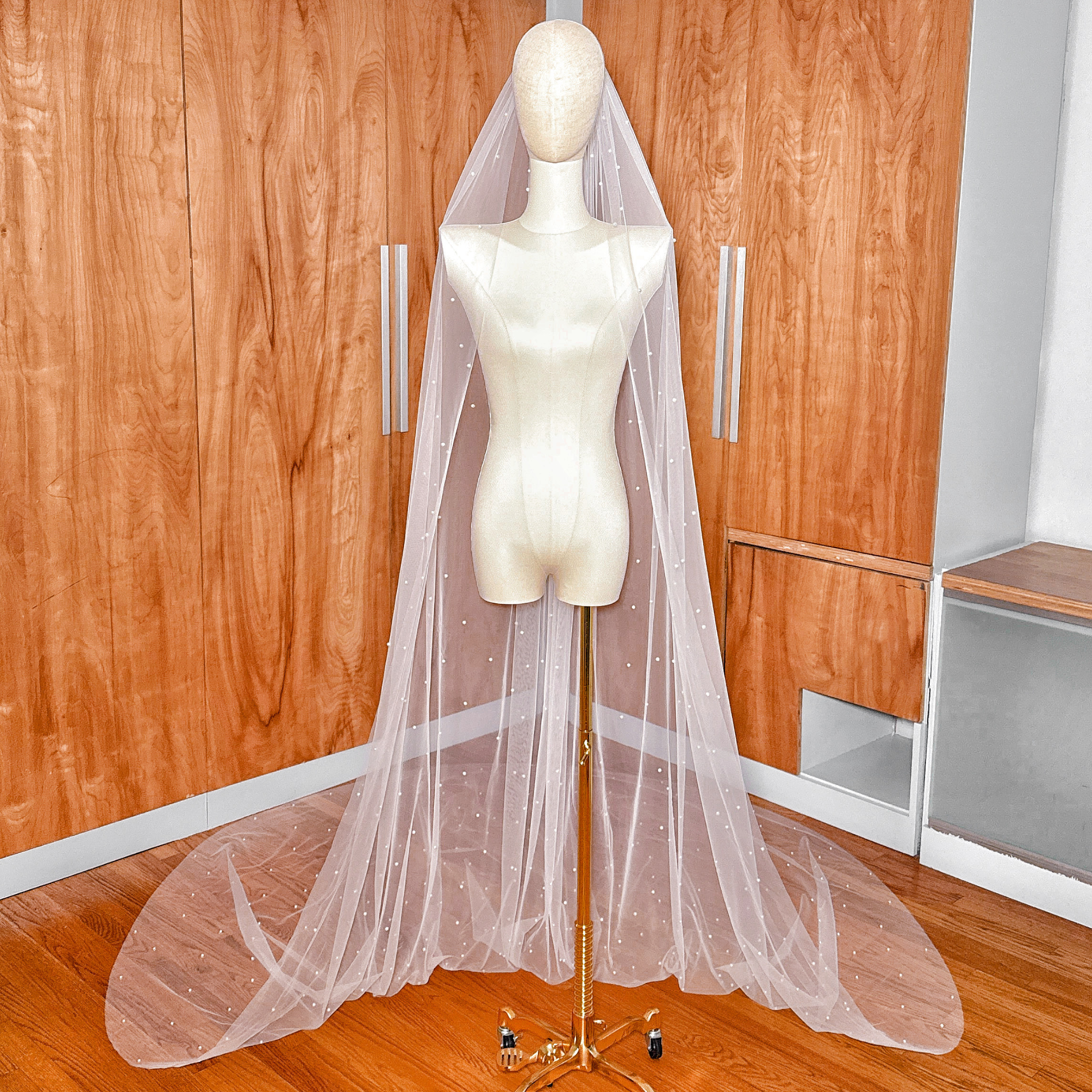Full-length view of a sheer ivory scattered pearl cathedral wedding veil cascading down a display.