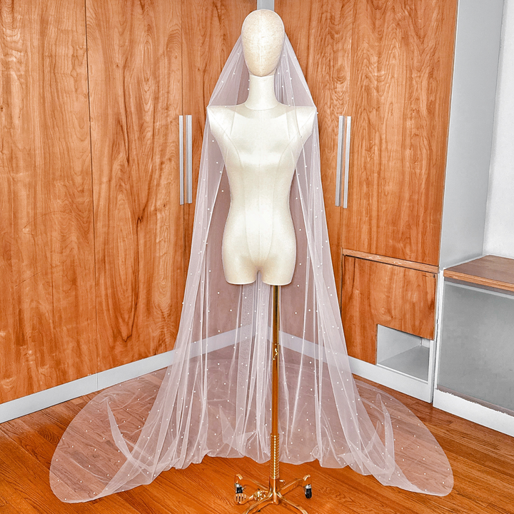 Full-length view of a sheer ivory scattered pearl cathedral wedding veil cascading down a display.