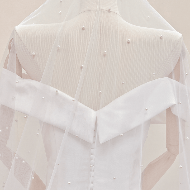 Detailed texture shot of various sized pearls scattered on an ivory cathedral bridal veil.
