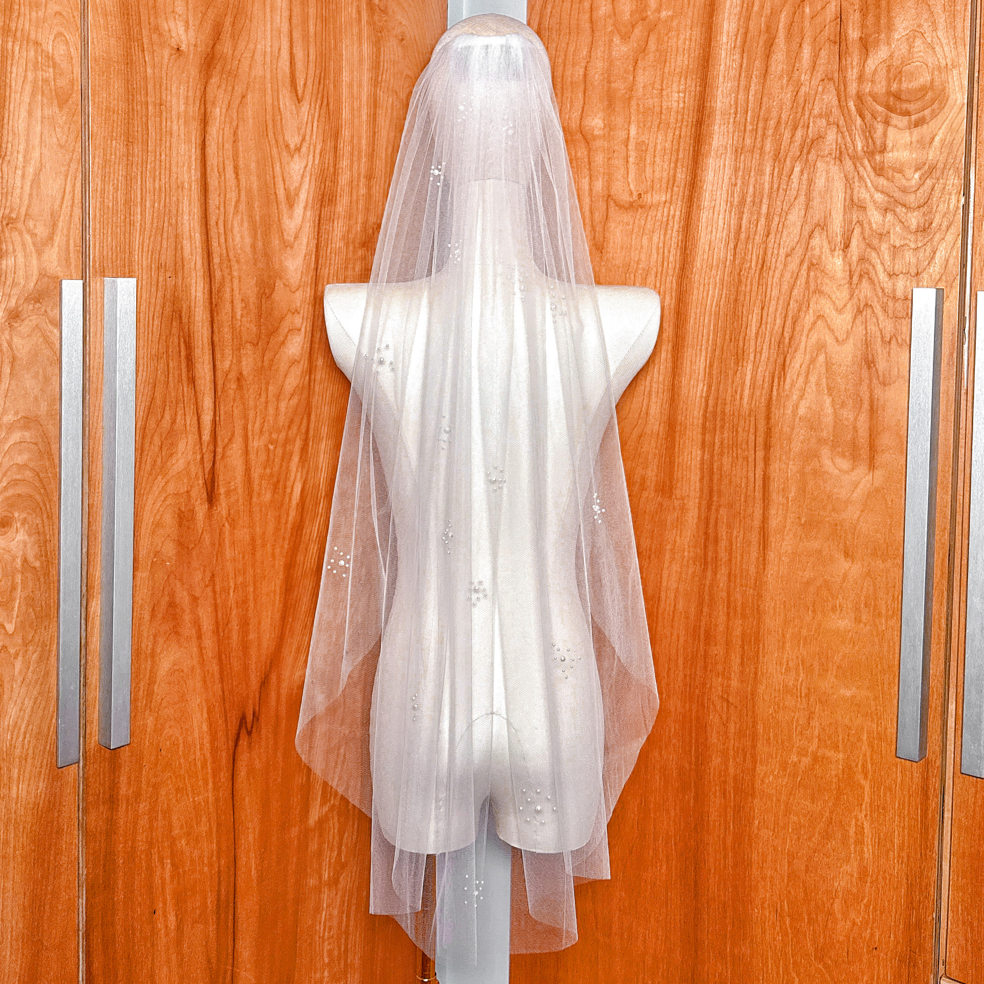 A bridal accessory featuring a pearl cluster wedding veil in fingertip length with a gathered comb attachment for a secure and voluminous look.
