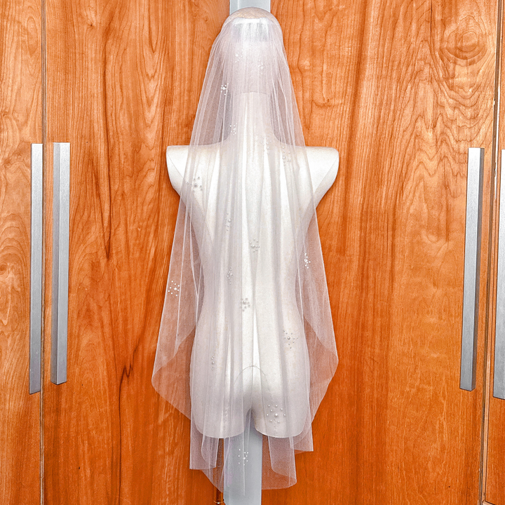 A bridal accessory featuring a pearl cluster wedding veil in fingertip length with a gathered comb attachment for a secure and voluminous look.
