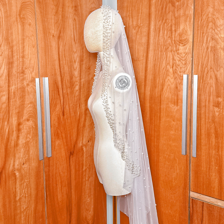 Close up of scattered pearls on the edge of a cathedral length mantilla wedding veil displayed on a bridal mannequin.