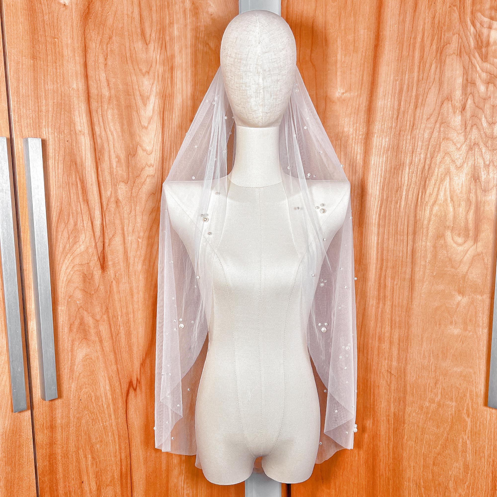 A fingertip-length bridal veil featuring delicate scattered pearls on soft ivory tulle, draped to show its elegant mid-length cut.