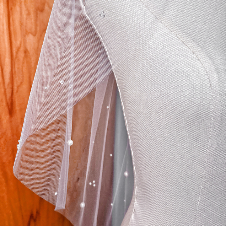 Close-up of hand-placed pearls on a sheer tulle scattered pearl wedding veil in elbow length.