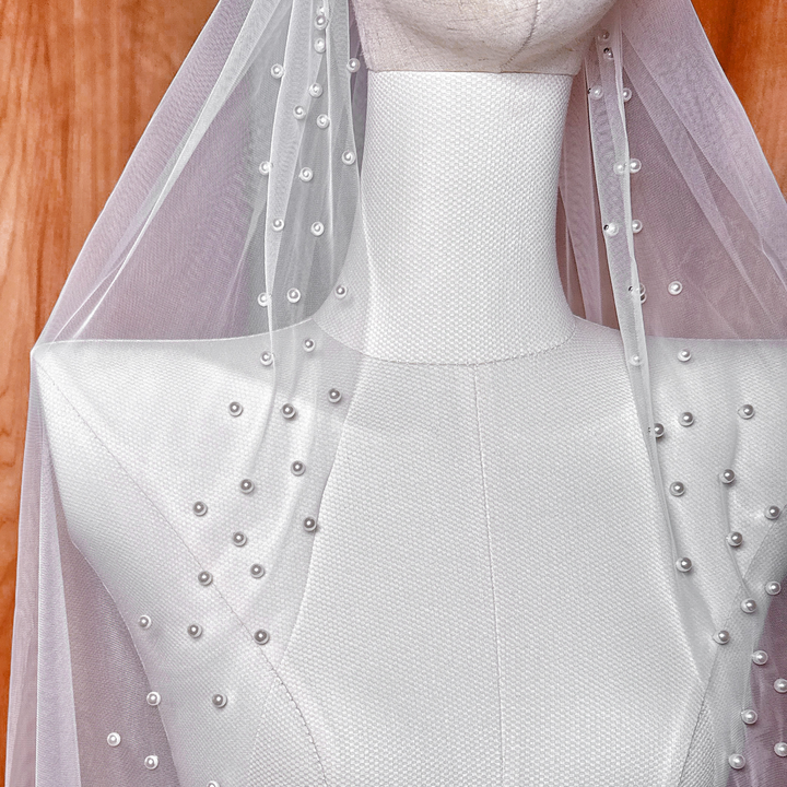Close-up of a sheer fingertip wedding veil featuring hand-placed pearls along the edge for a classic bridal look.