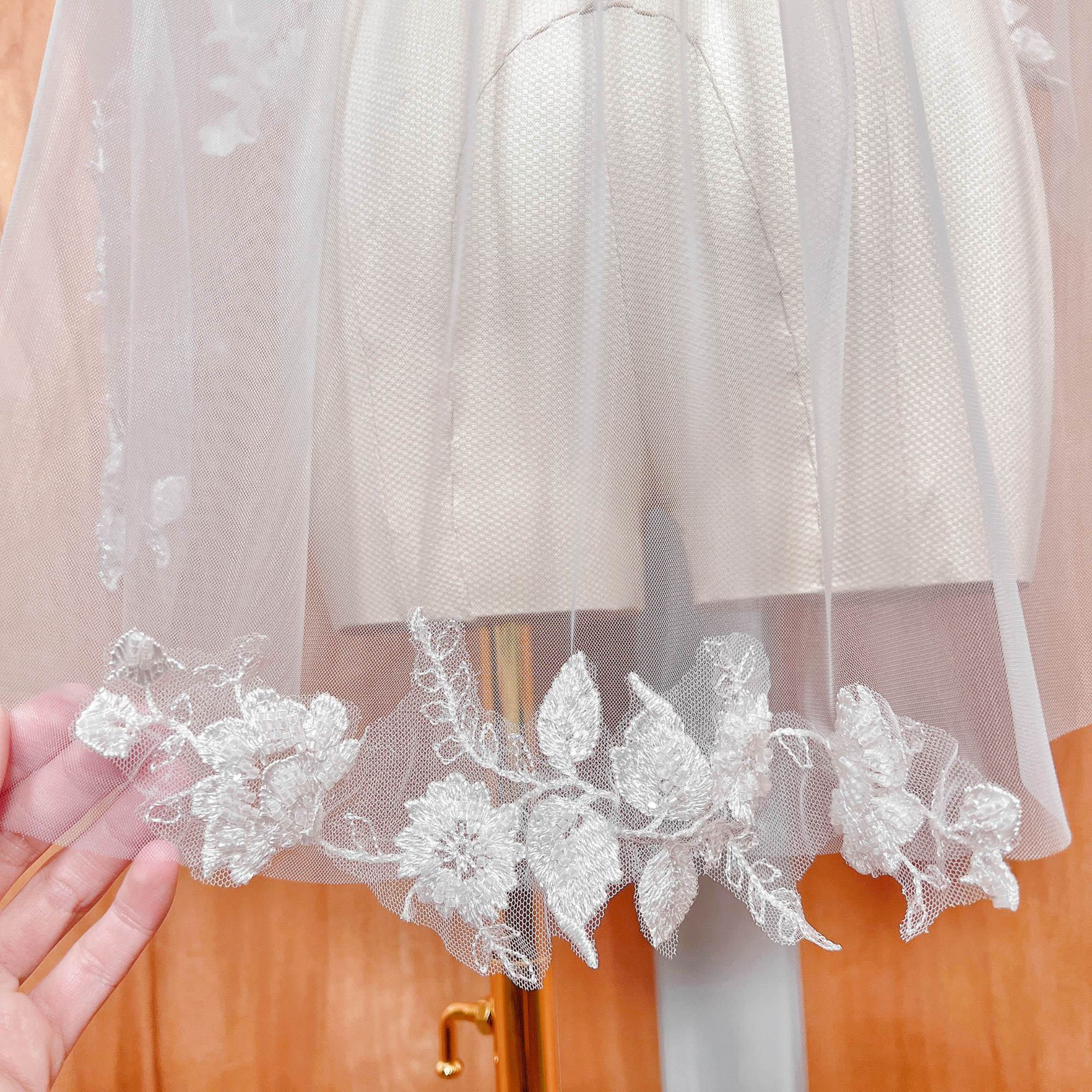 Sheer fingertip length floral beaded lace wedding veil with a soft tulle drape on a mannequin.