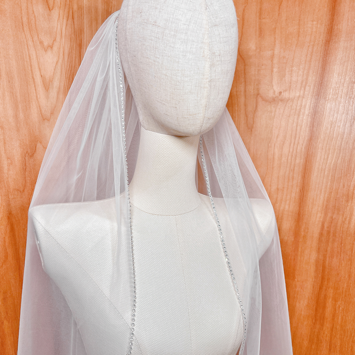 Side profile showing the elegant drape of a rhinestone edge wedding veil in fingertip length.