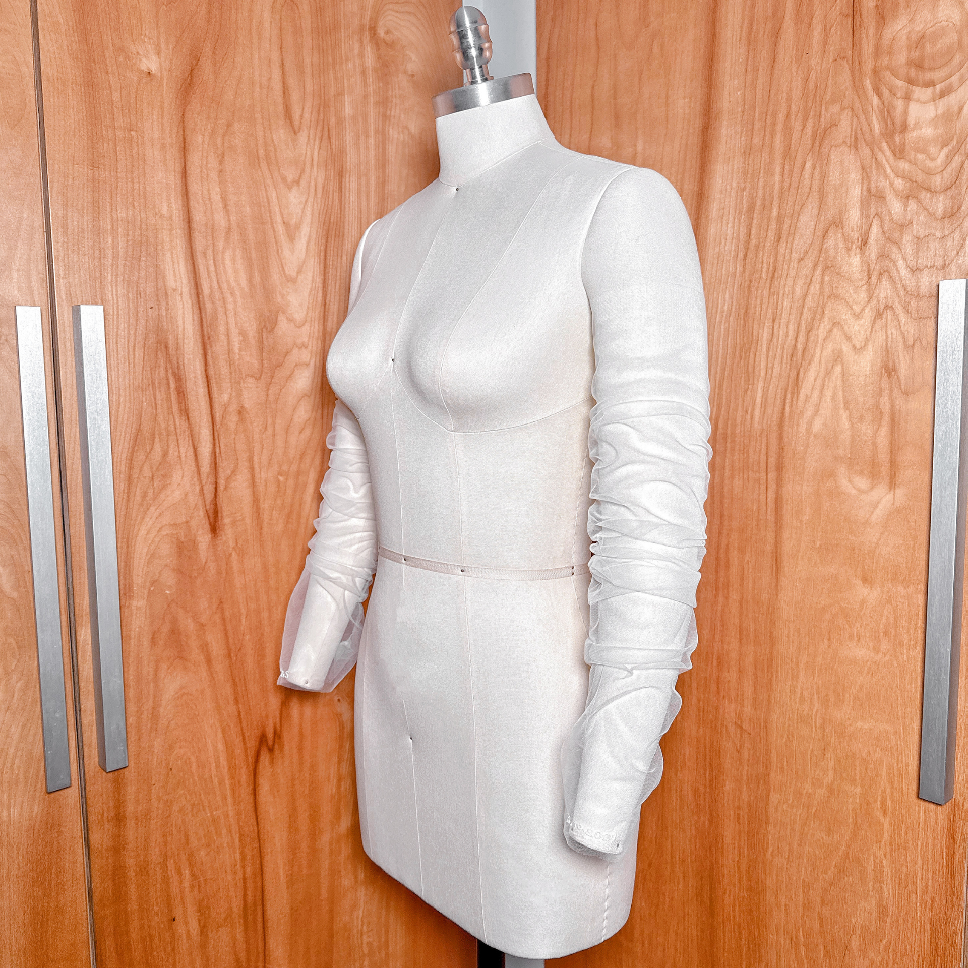 A close-up view of sheer white ruched tulle detachable bridal sleeves displayed on a mannequin against a natural wood closet background.