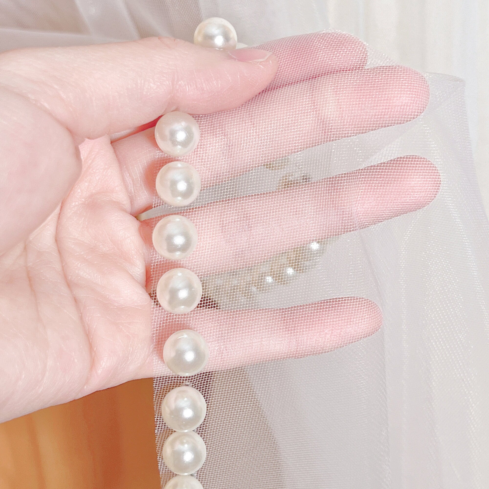 Close-up detail of hand-sewn pearls along the finished edge of a sheer tulle wedding veil.