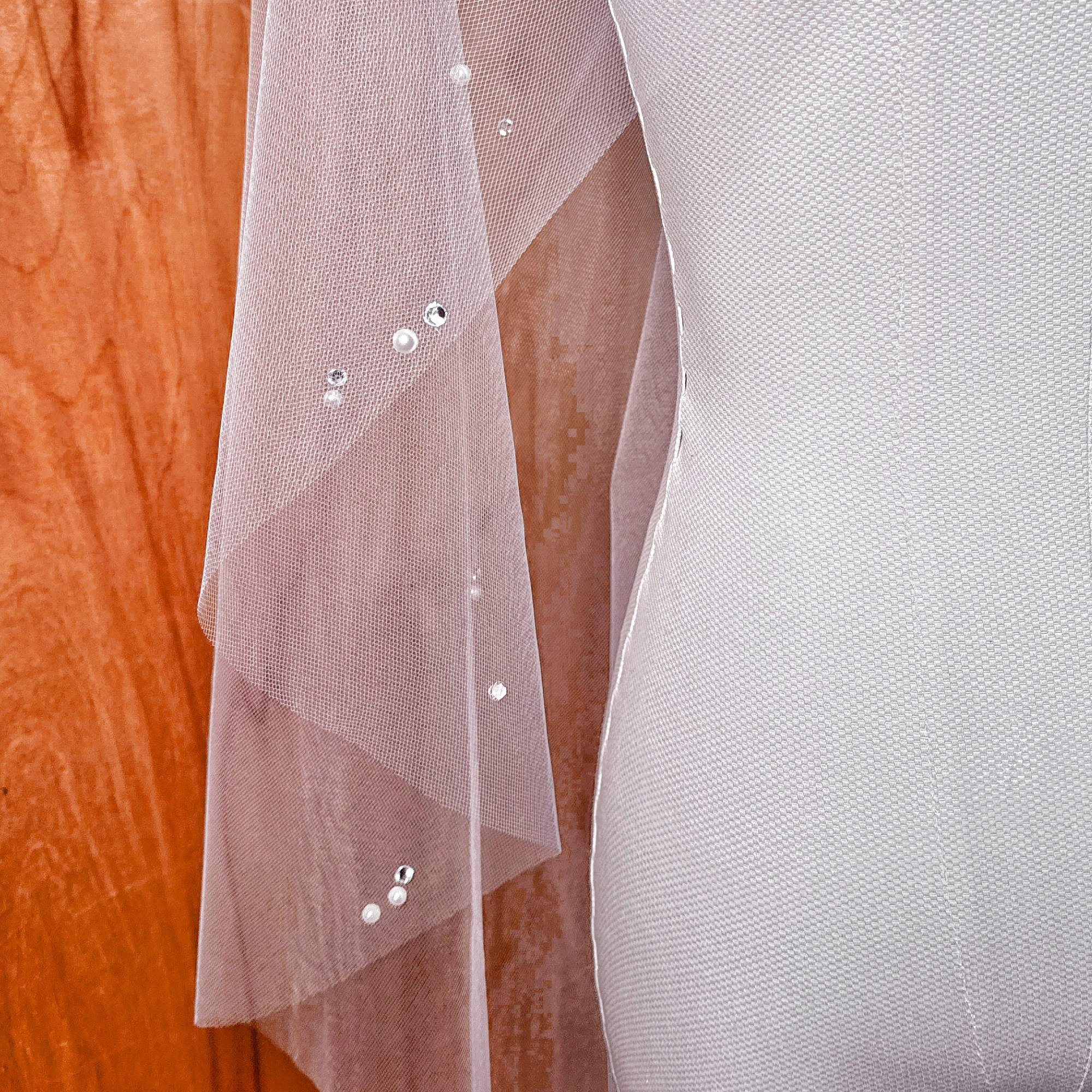 Close-up detail of the hand-placed pearls and shimmering rhinestones on a sheer tulle bridal veil.