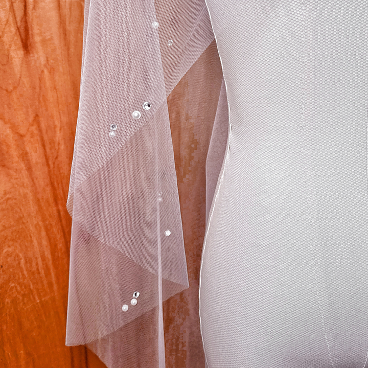 Close-up detail of the hand-placed pearls and shimmering rhinestones on a sheer tulle bridal veil.