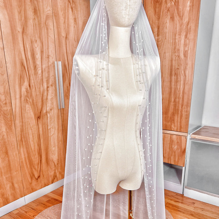 Side profile of the Scattered Pearl Edge Wedding Veil draped in a long cathedral length, highlighting the sheer bridal tulle and pearl accents.