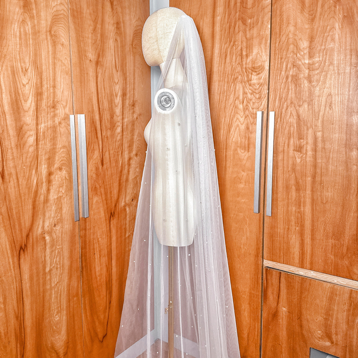 A cathedral-length scattered pearl wedding veil gathered at the top and attached to a secure silver bridal comb.
