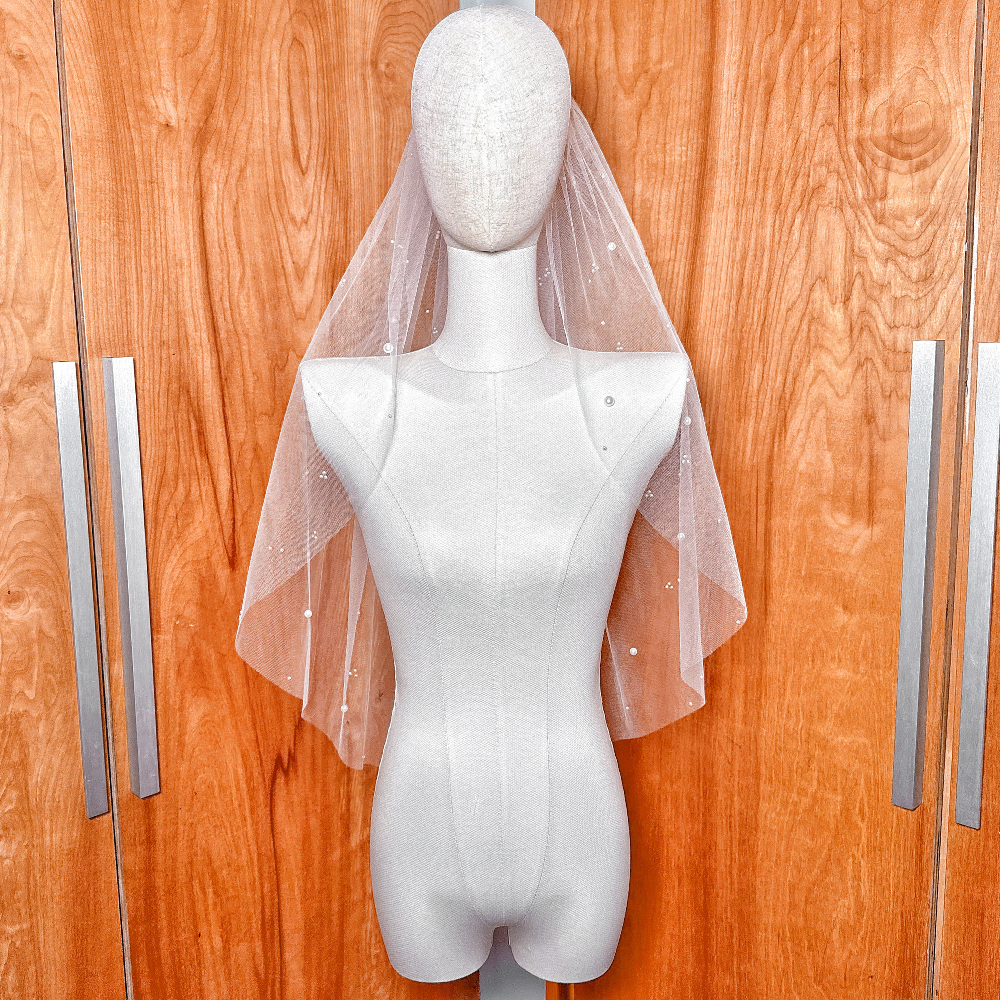 Elbow length wedding veil made of sheer tulle with delicate scattered pearls for a modern bridal look.