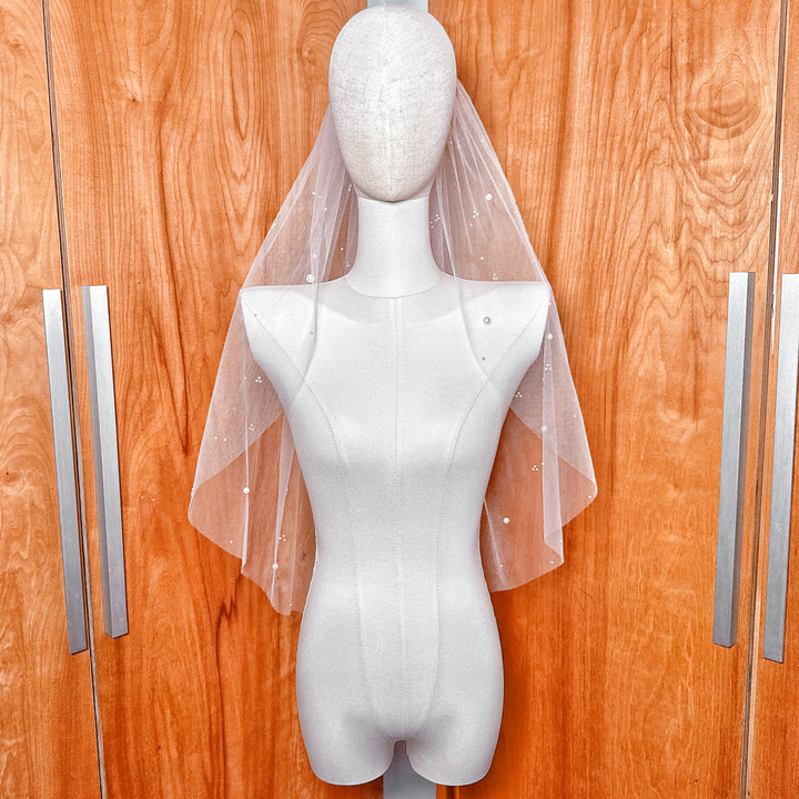 Elbow length wedding veil made of sheer tulle with delicate scattered pearls for a modern bridal look.