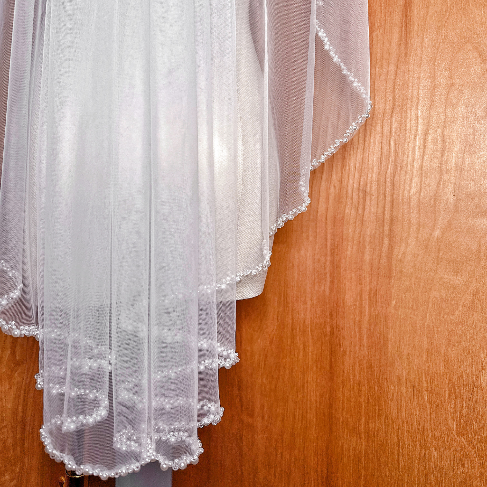 High-resolution texture shot of the sheer bridal illusion tulle and pearl embroidery on a cascading fingertip length veil.