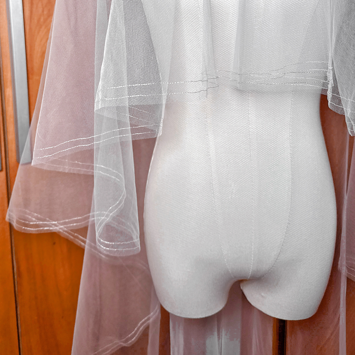 High-resolution view of the sheer bridal tulle and silver metallic edge on a waltz length two tier veil with blusher.
