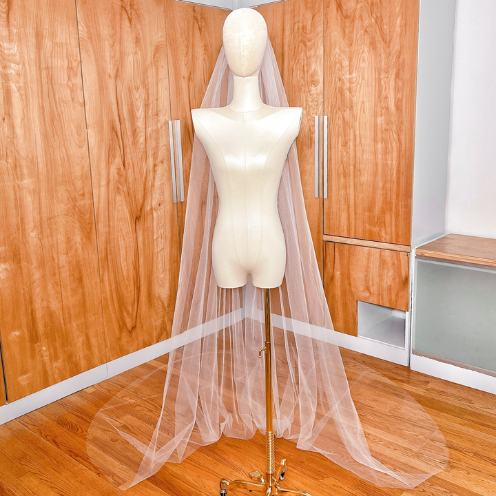 Detailed shot of the lightweight, sheer texture of a simple cathedral tulle wedding veil with a classic raw edge design.