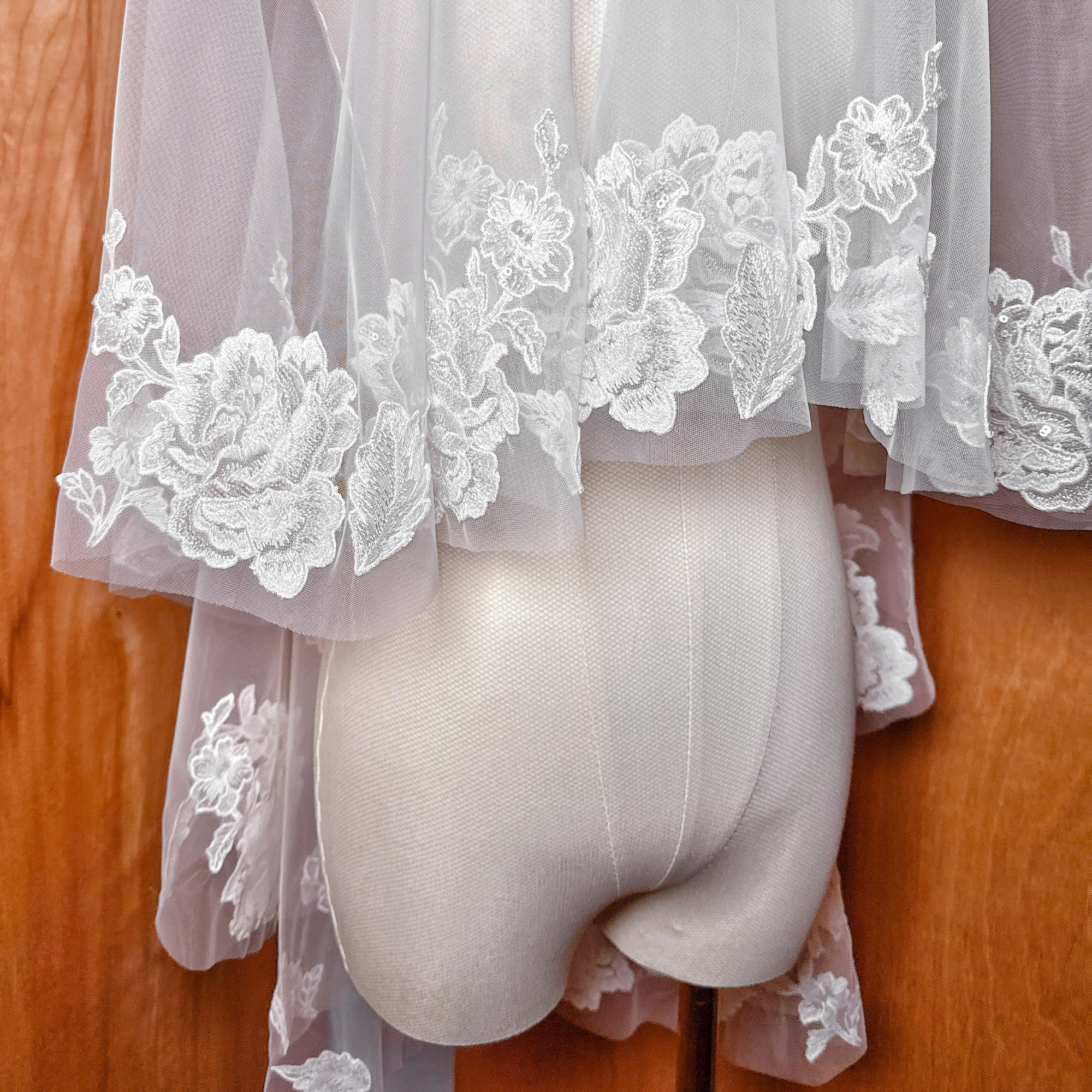 Sheer fabric texture of a two tier floral lace wedding veil, fingertip length display.