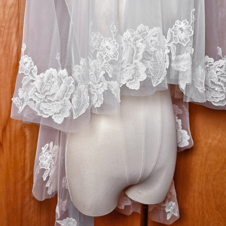 Sheer fabric texture of a two tier floral lace wedding veil, fingertip length display.