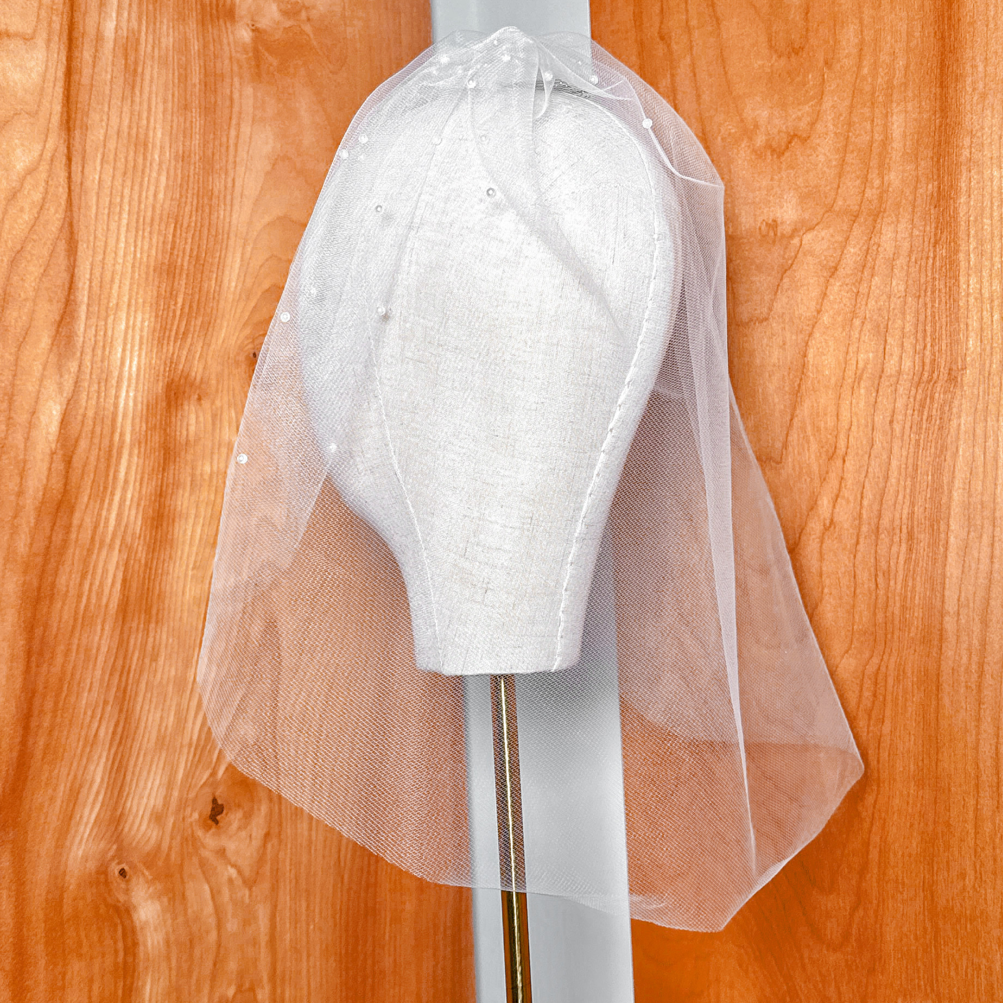 Side view of a sheer pearl birdcage wedding veil showing gathering and comb attachment.