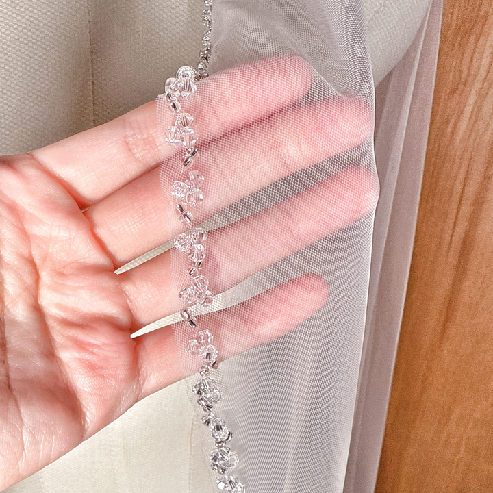 Side profile showing the sheer tulle fabric and waltz length of the crystal beaded edge wedding veil.