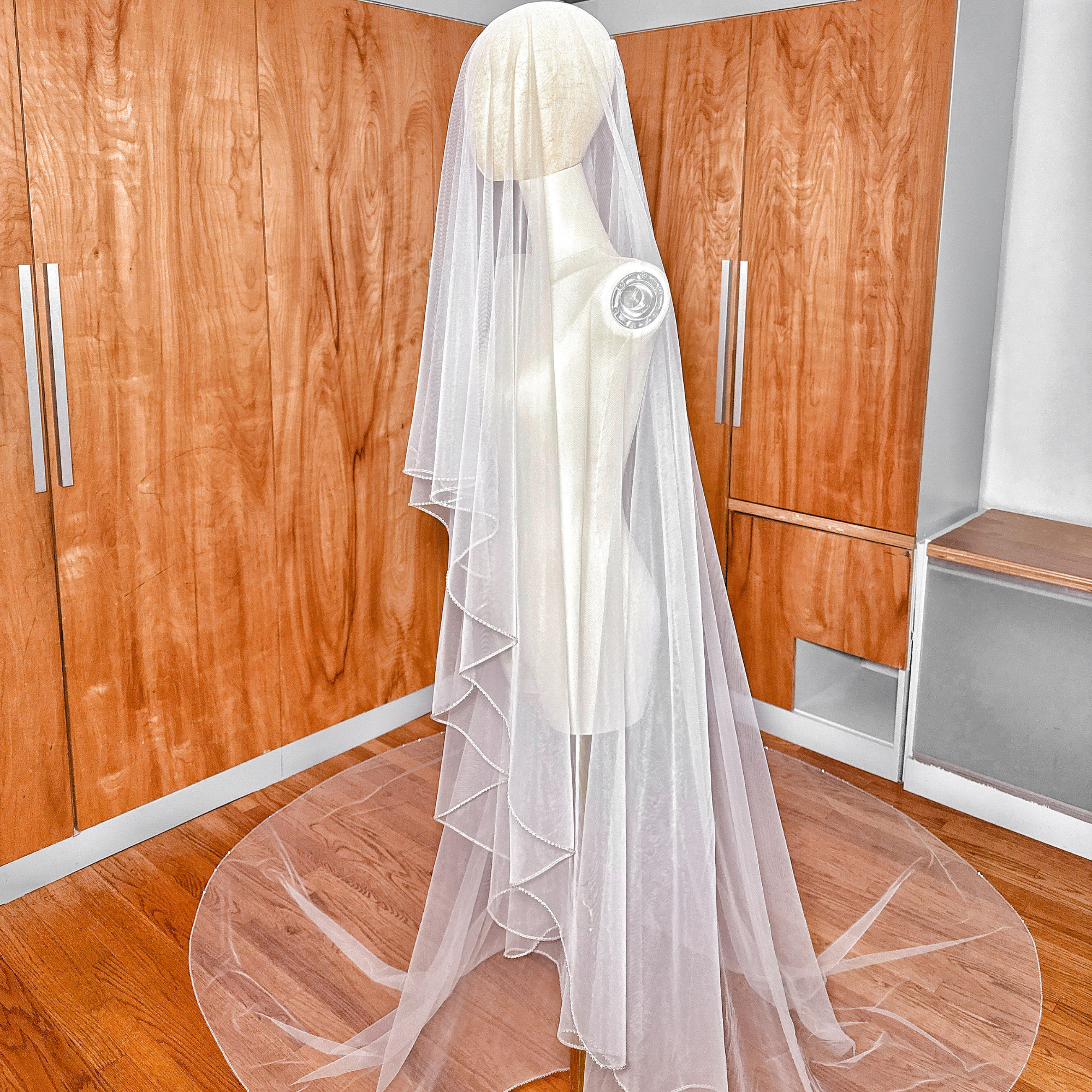 Side profile image showcasing the dramatic drape and blusher layer of a two-tier cathedral wedding veil with rhinestone trim.
