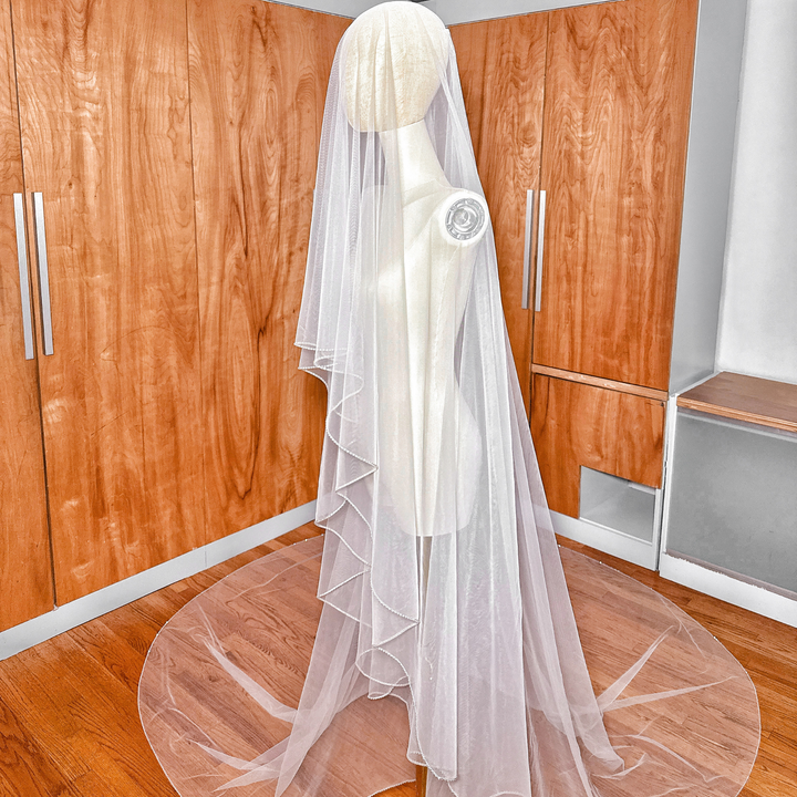 Side profile image showcasing the dramatic drape and blusher layer of a two-tier cathedral wedding veil with rhinestone trim.