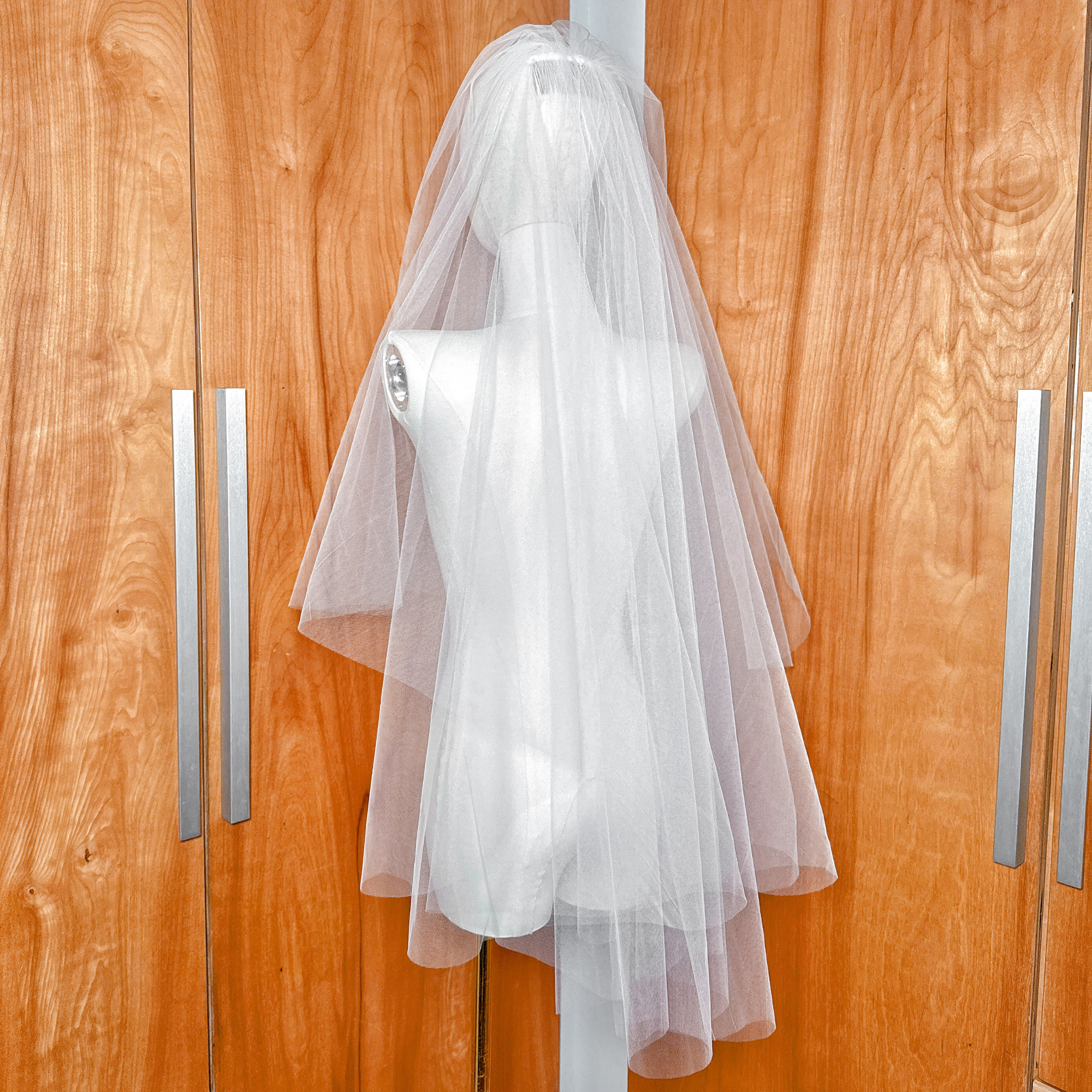Side profile of a voluminous two tier fingertip length blusher veil on a mannequin showing layered tulle volume.