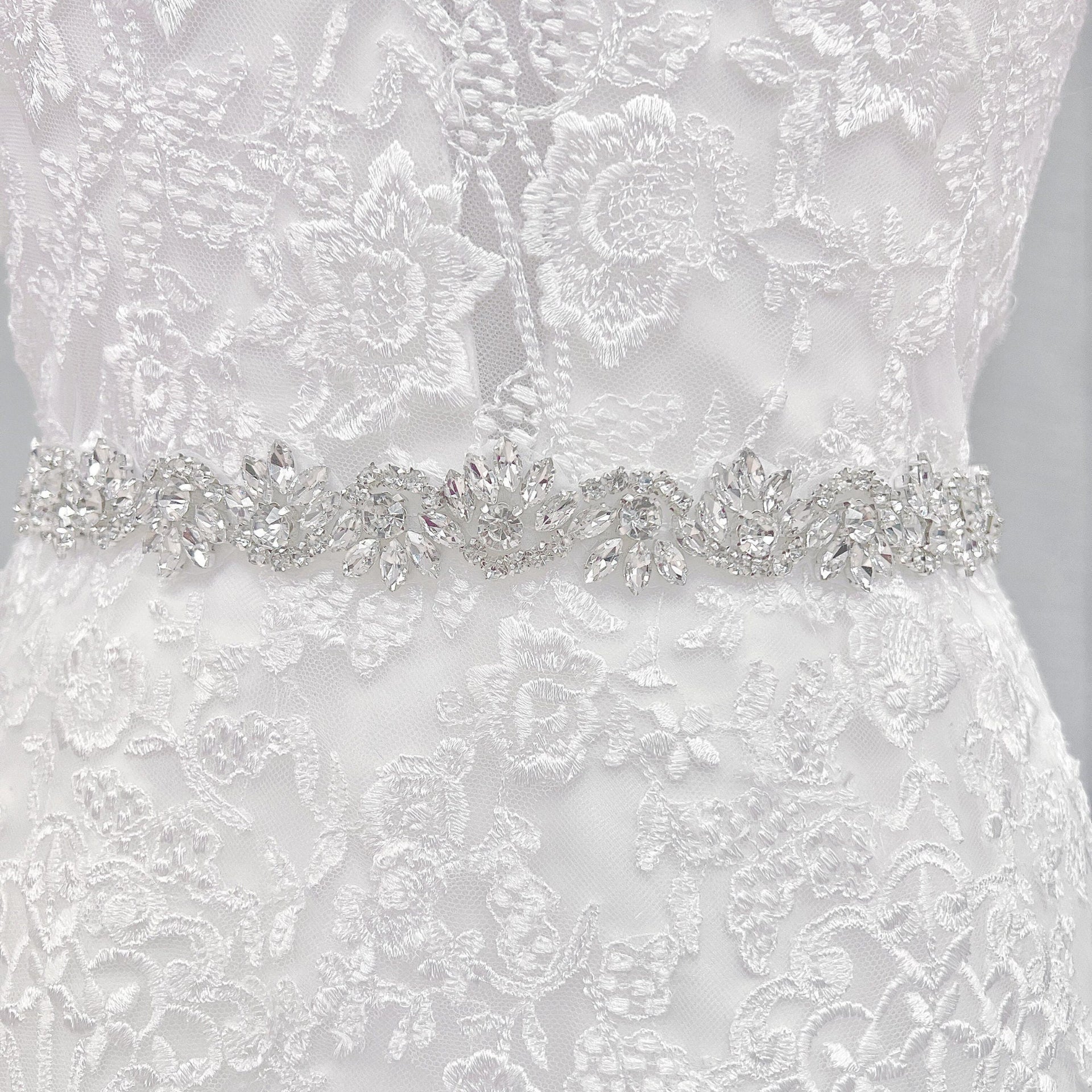 A close-up shot of a silver beaded bridal belt with intricate crystal rhinestones on a mannequin display.