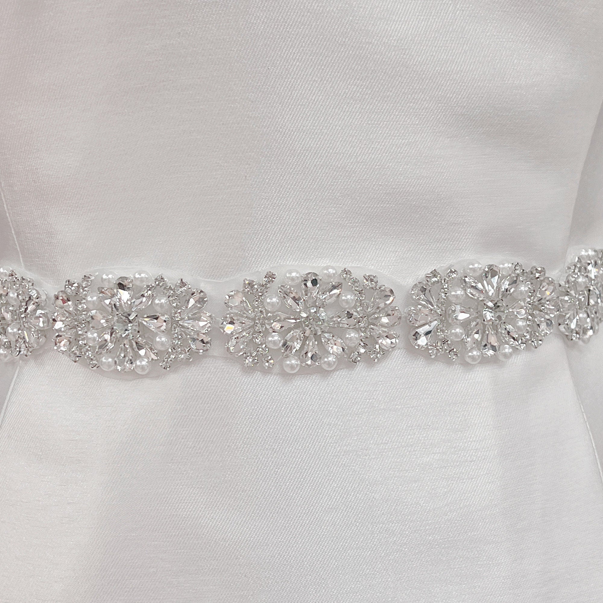 Close-up of a silver rhinestone and pearl bridal belt with intricate beadwork detailing on a dress display.