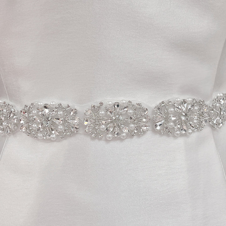 Close-up of a silver rhinestone and pearl bridal belt with intricate beadwork detailing on a dress display.