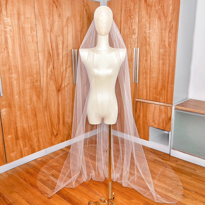 Front view of a simple cathedral tulle wedding veil with a raw edge, showing the sheer fabric draping elegantly from a bridal comb.