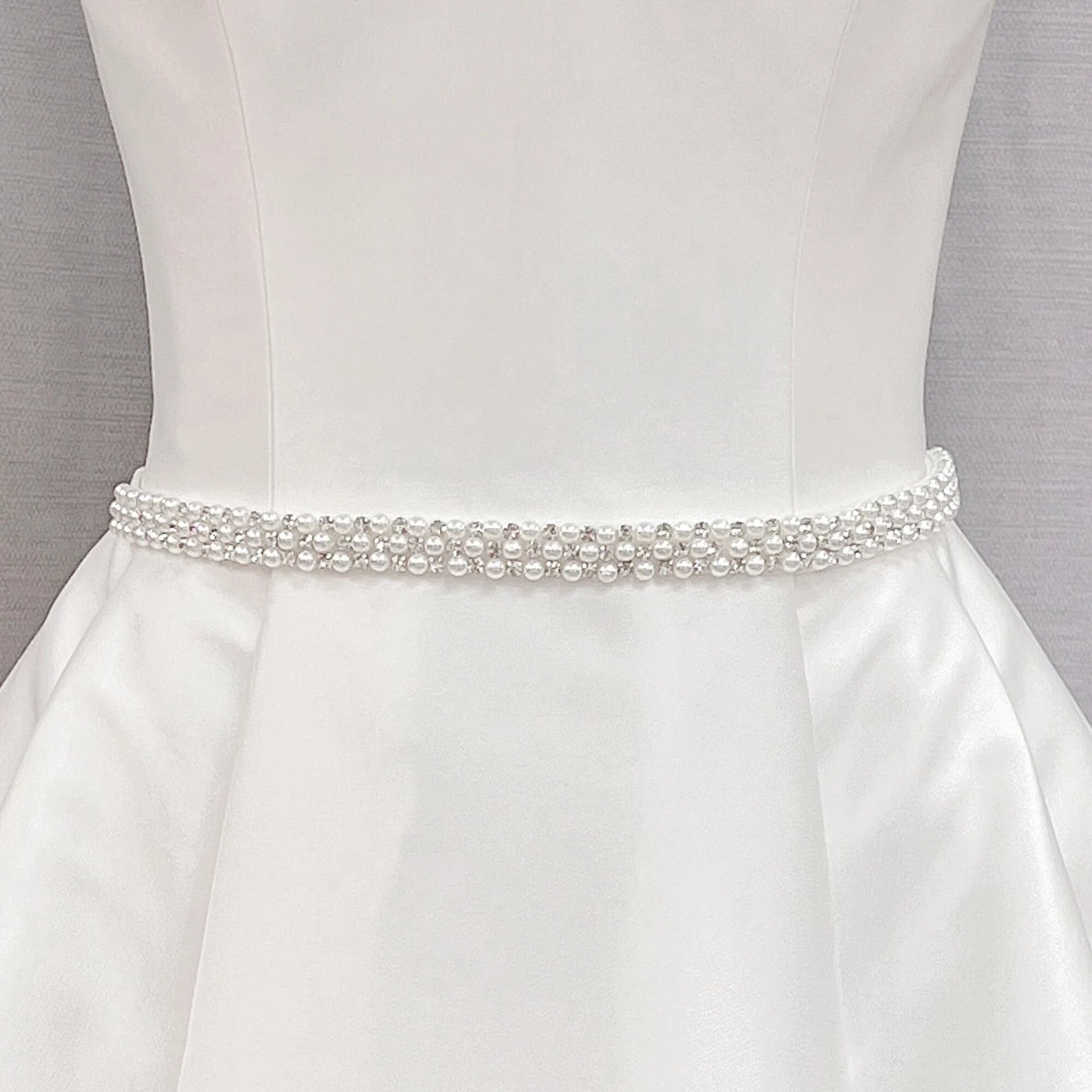 Simple rhinestone and pearl bridal belt with crystals and ivory beads displayed on a white dress mannequin.