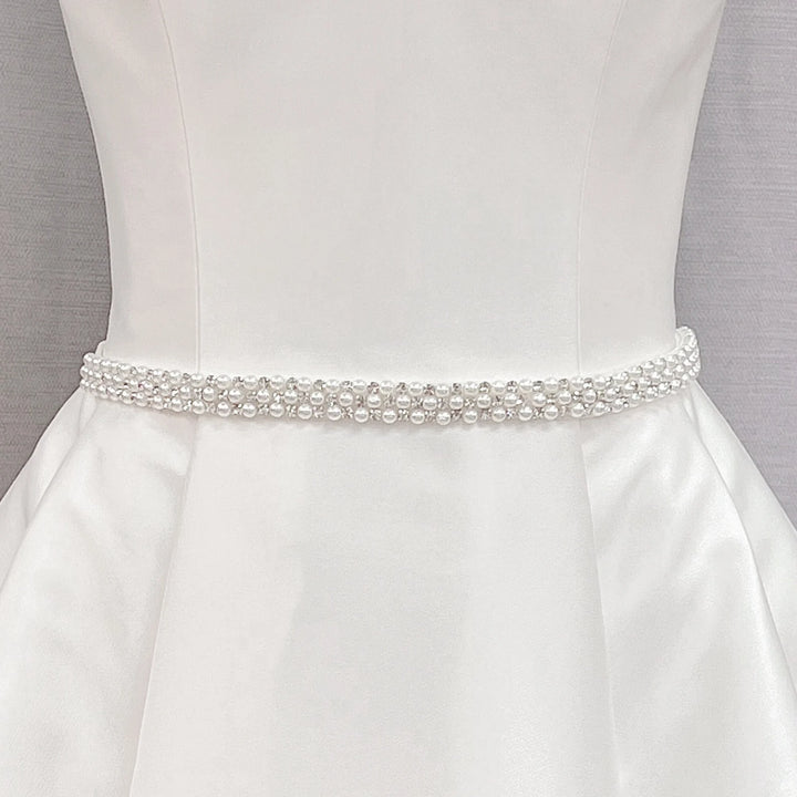 Simple rhinestone and pearl bridal belt with crystals and ivory beads displayed on a white dress mannequin.